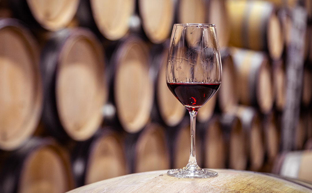 A glass of wine stood on a barrel, with more barrels in the background