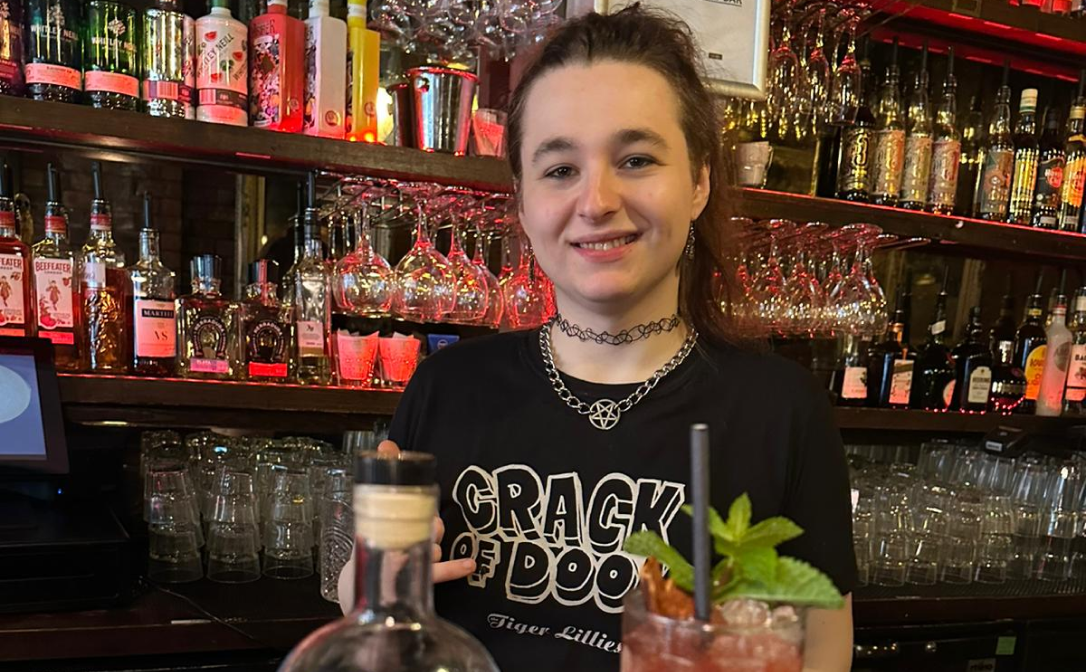 A person serving a cocktail behind a bar counter