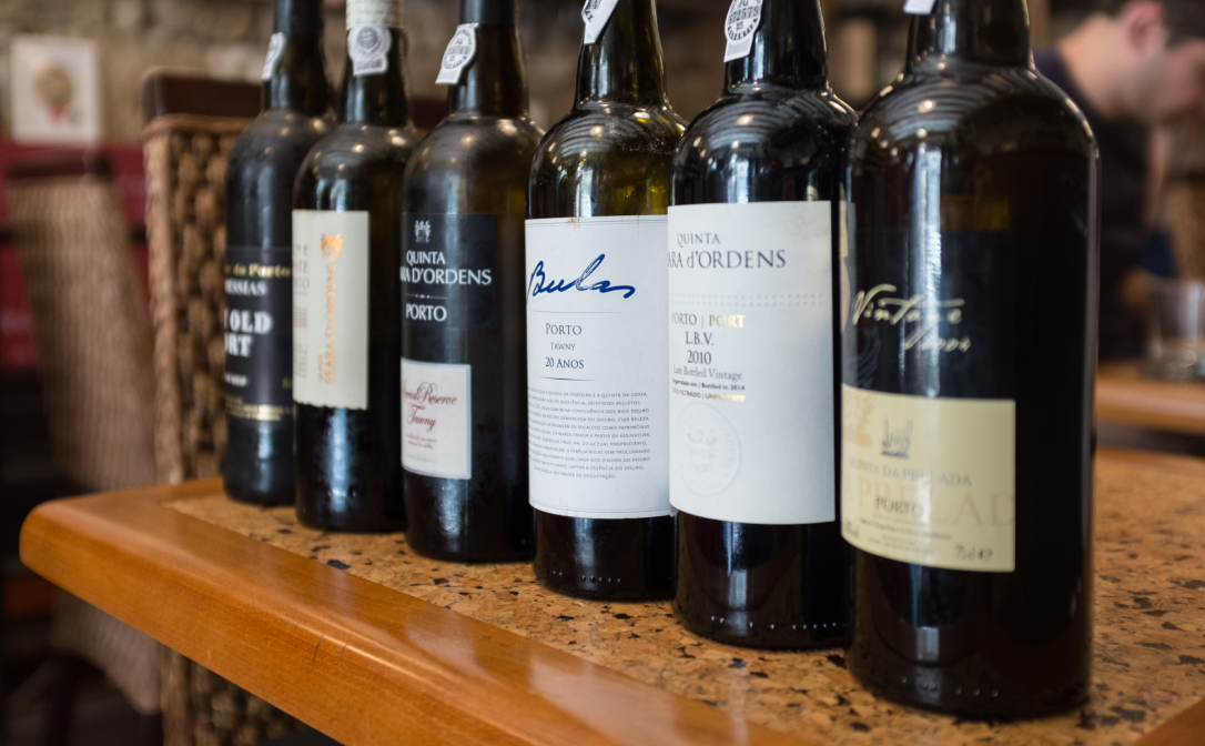 Glass bottles of Port from different producers lined up on a wooden shelf
