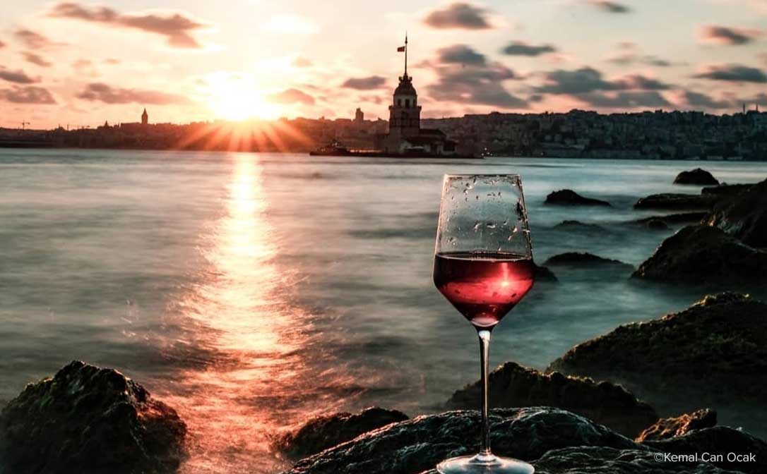 Kemal Can Ocak. Red wine on rocks, overlooking the sun setting over the sea