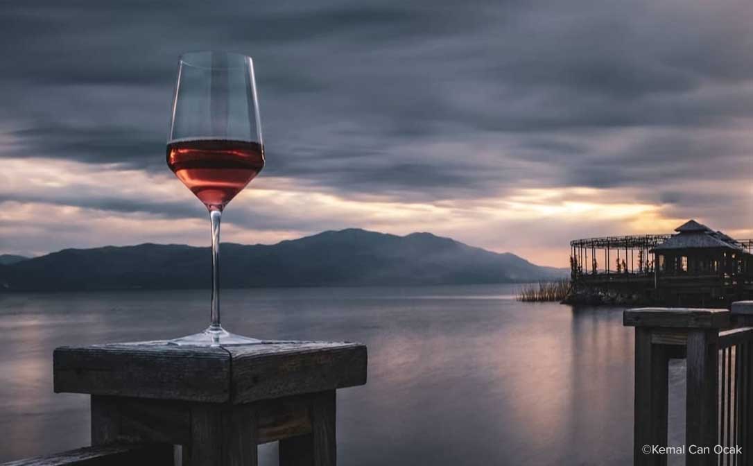 Photograph by Kemal Can Ocak. Red wine on a wooden post, overlooking tranquil waters